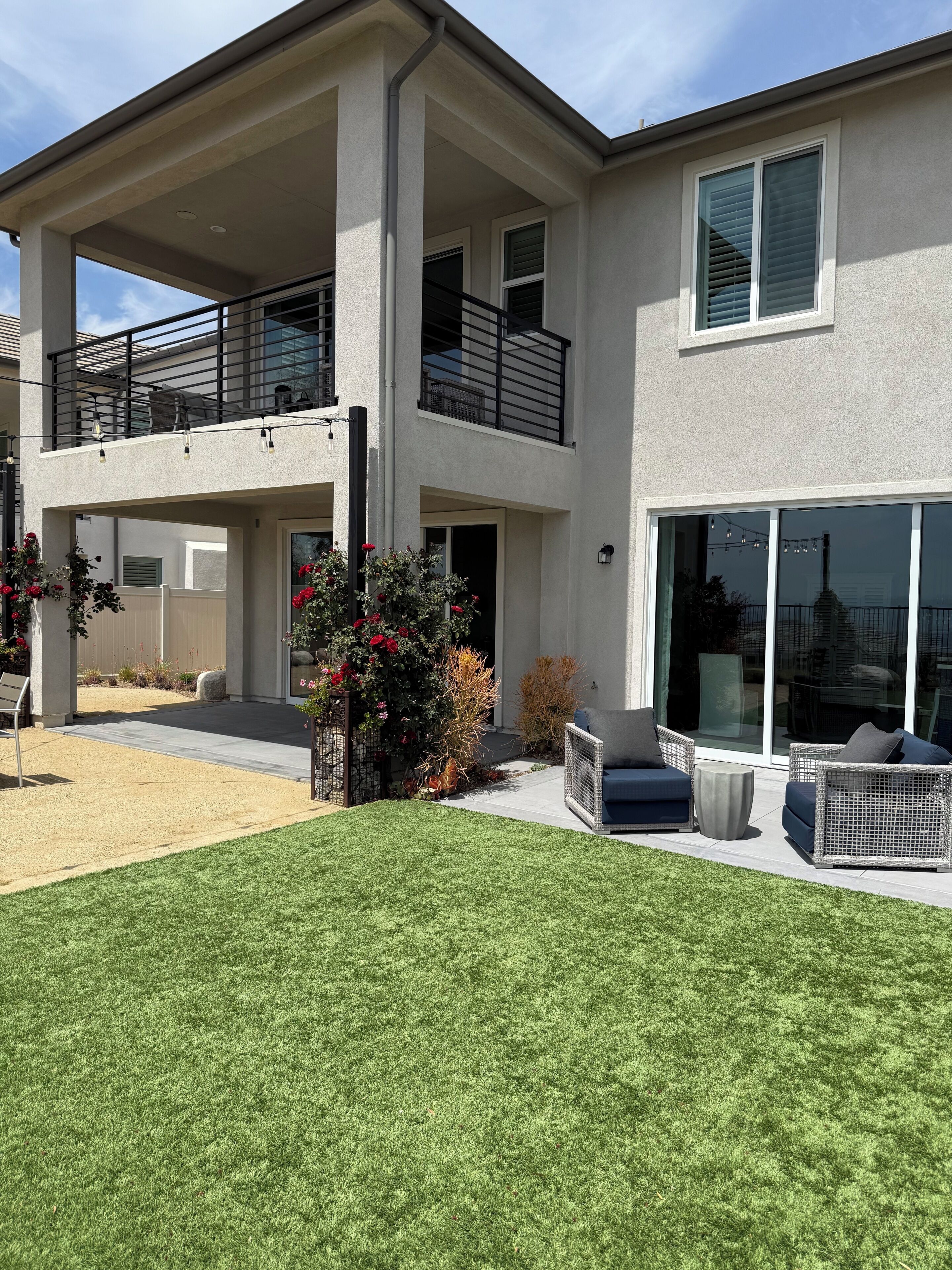 Una casa de dos pisos con un balcón, un patio con muebles de exterior y un césped bien cuidado.