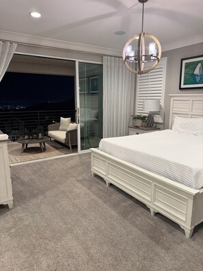 A bedroom with a large bed, a glass door leading to a balcony, a ceiling light, and a framed picture on the wall.