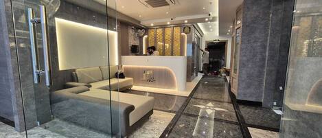 A modern hotel lobby with a reception desk, seating area, and a glass partition.