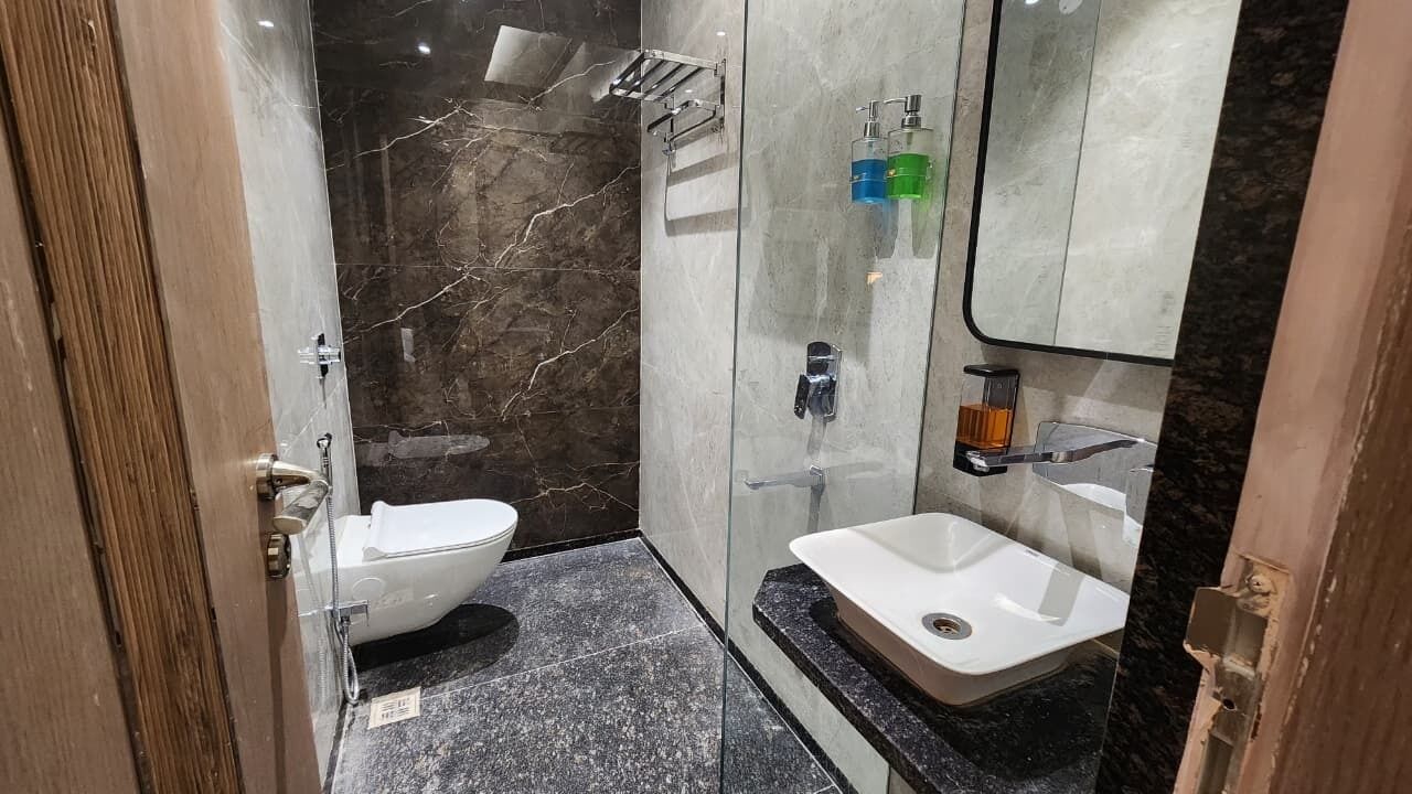 Un baño moderno con ducha de mármol, inodoro blanco y lavamanos con espejo.