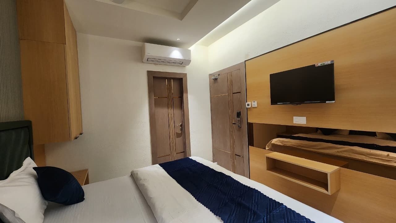 A hotel room with a bed, a TV mounted on the wall, wooden wardrobes, and an air conditioning unit.