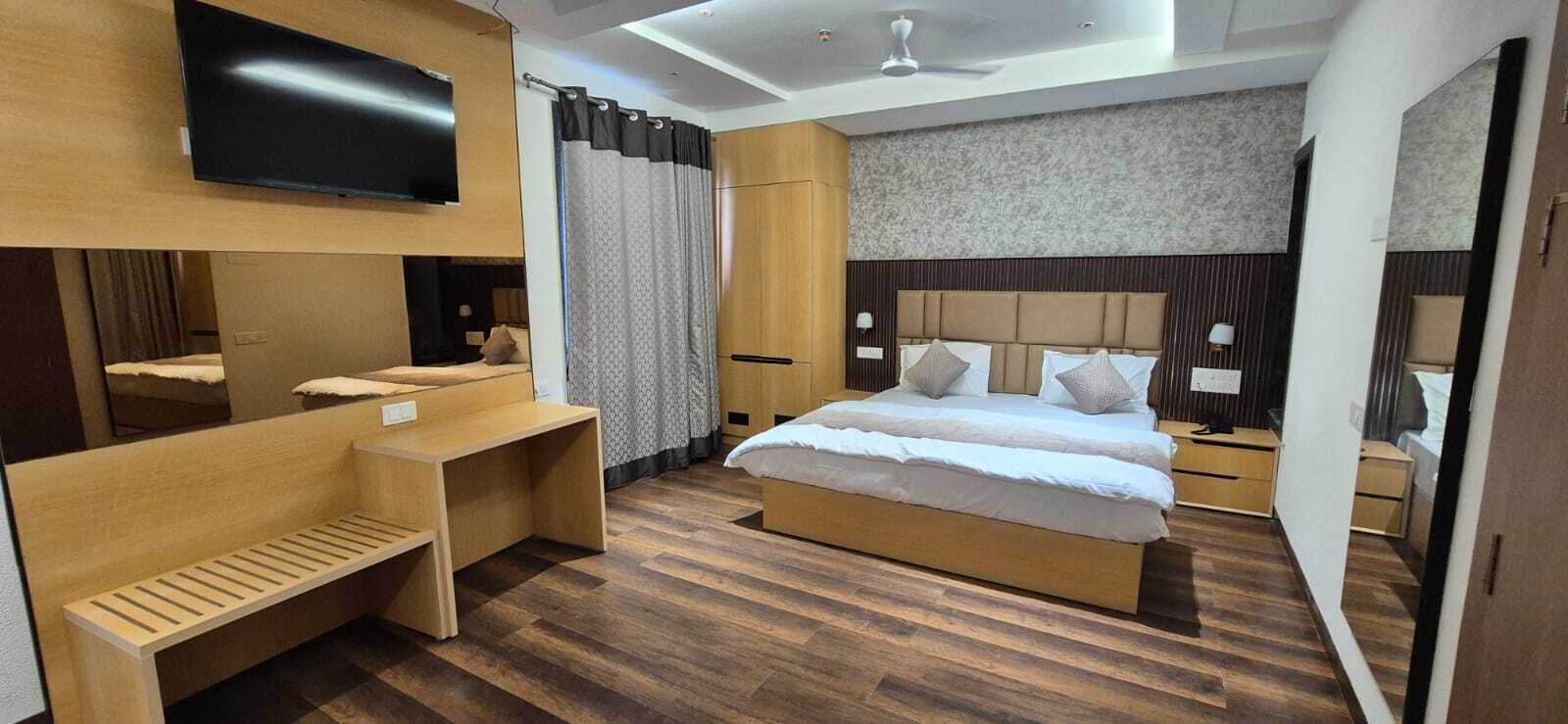 A modern hotel room with a large bed, a desk, a flat-screen TV, and a ceiling fan.