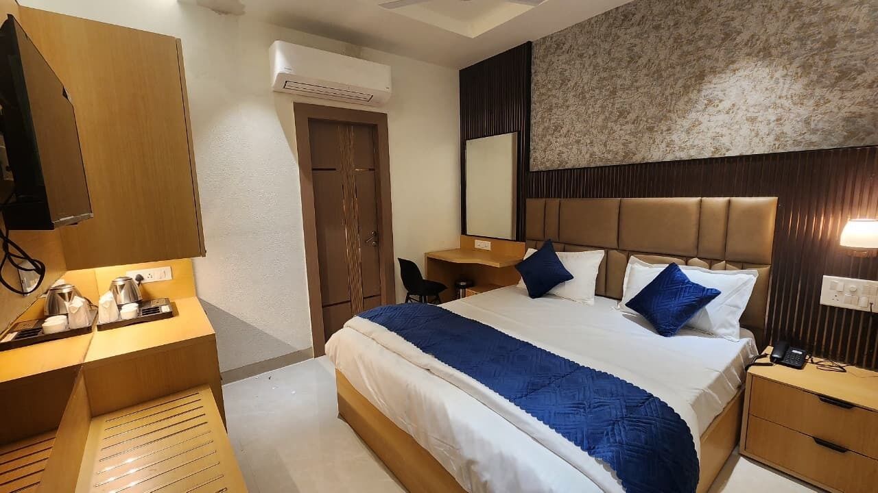 A hotel room with a bed, bedside table, desk, chair, and an air conditioning unit.