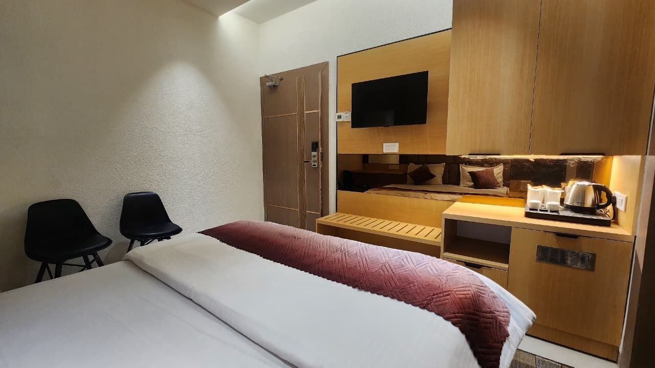 Ett hotellrum med en säng, två stolar, ett skrivbord med en tv och ett litet kök.