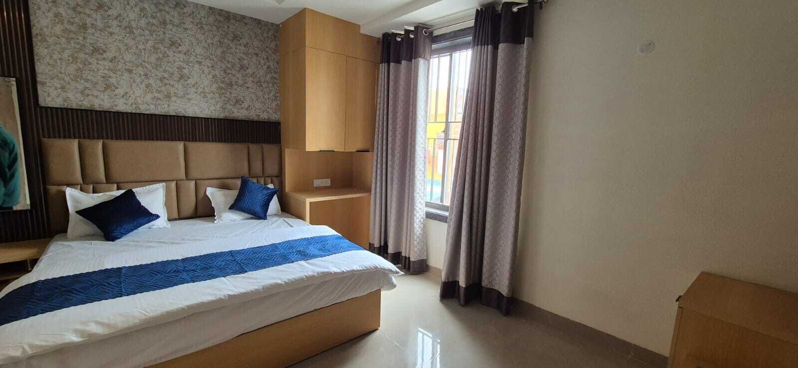 Ein Hotelzimmer mit Bett, Kopfteil, Nachttisch, Kleiderschrank und einem Fenster mit Vorhängen.