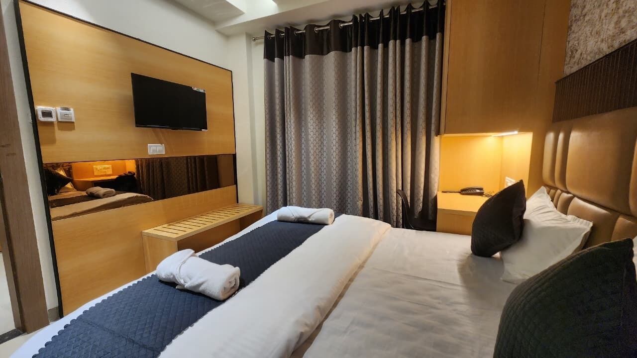A hotel room with a bed, bedside table, lamp, and a TV mounted on the wall.
