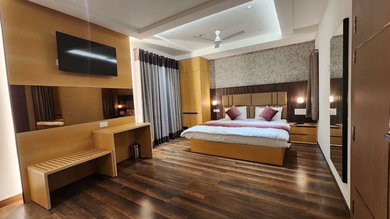 A modern hotel room with a large bed, a TV mounted on the wall, a desk, and a ceiling fan.