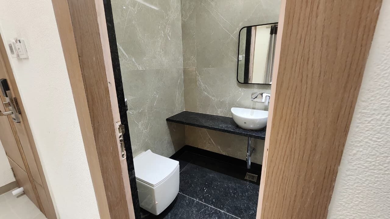 Et badeværelse med et hvidt toilet, en vask med et spejl over og et bruseområde med flisebeklædte vægge.