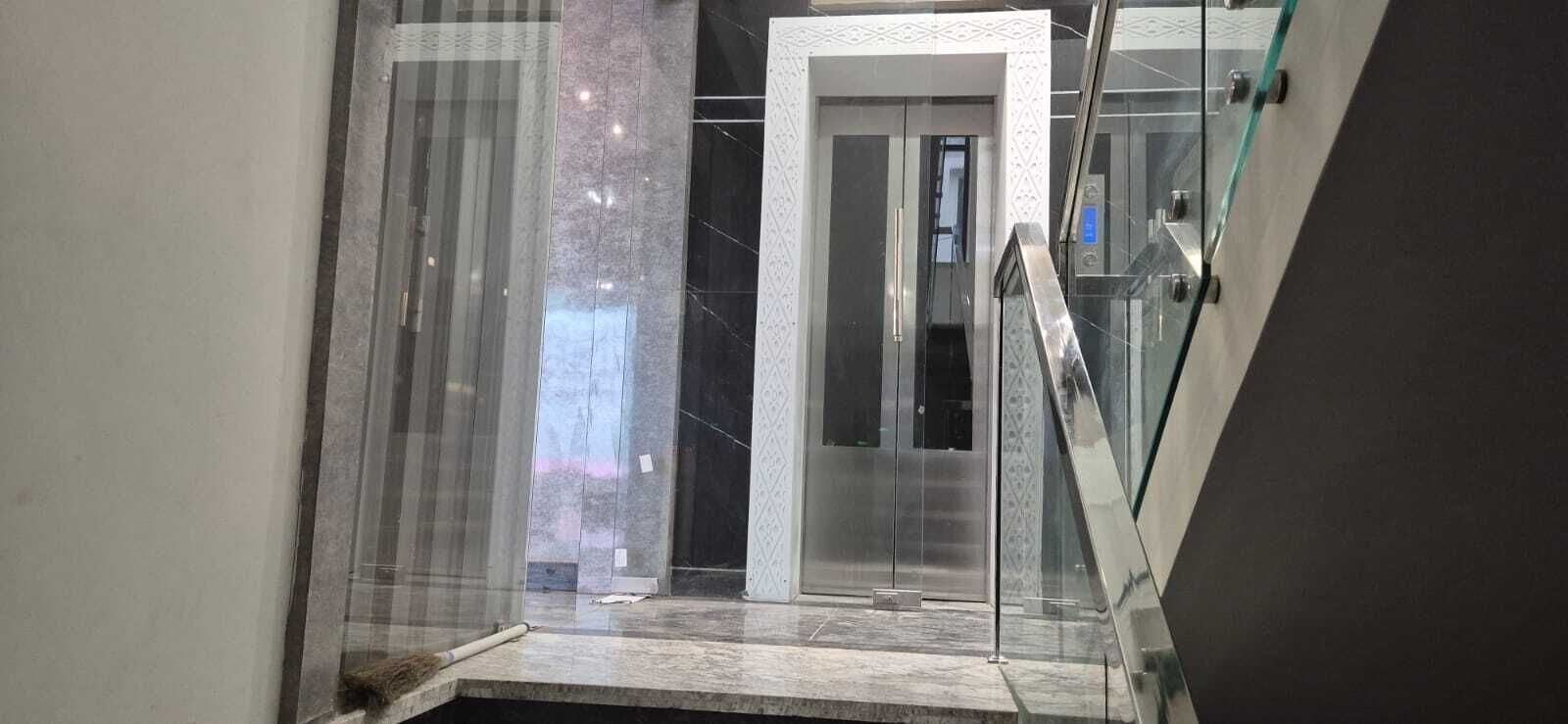 Un interior moderno con un ascensor de vidrio, una escalera de mármol y una puerta que da a otra habitación.