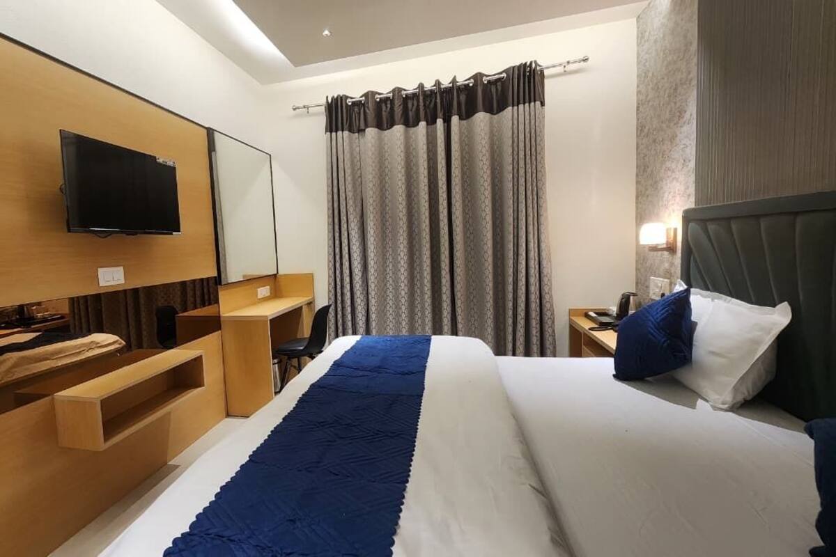 A modern hotel room with a bed, TV, wooden desk, and a large window with curtains.