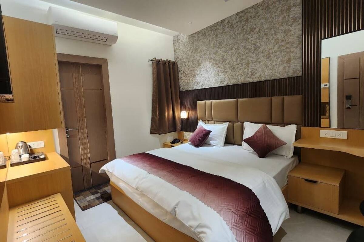 A hotel room with a bed, bedside table, TV, and a mirror.