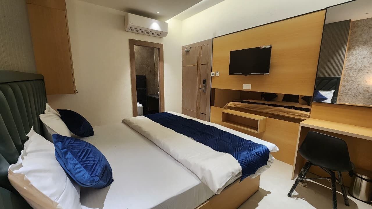 A hotel room with a bed, a desk, a chair, a TV, and a wardrobe.