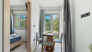 Ett sovrum med en säng, ett litet bord med stolar, ett fönster och utsikt över grönområden.