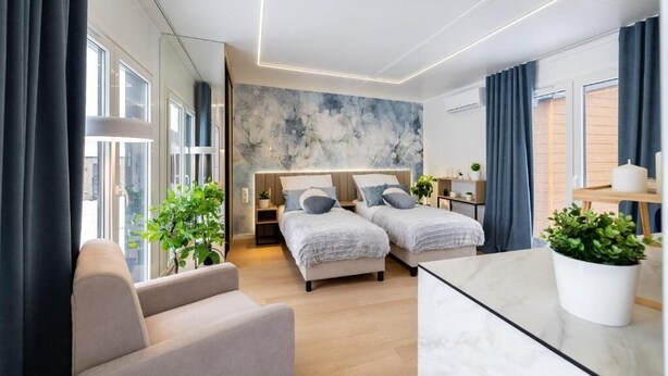 A modern hotel room with two beds, a sofa, a marble table, and a large window. - Studios an der Alten Post (Maxhütte-Haidhof)