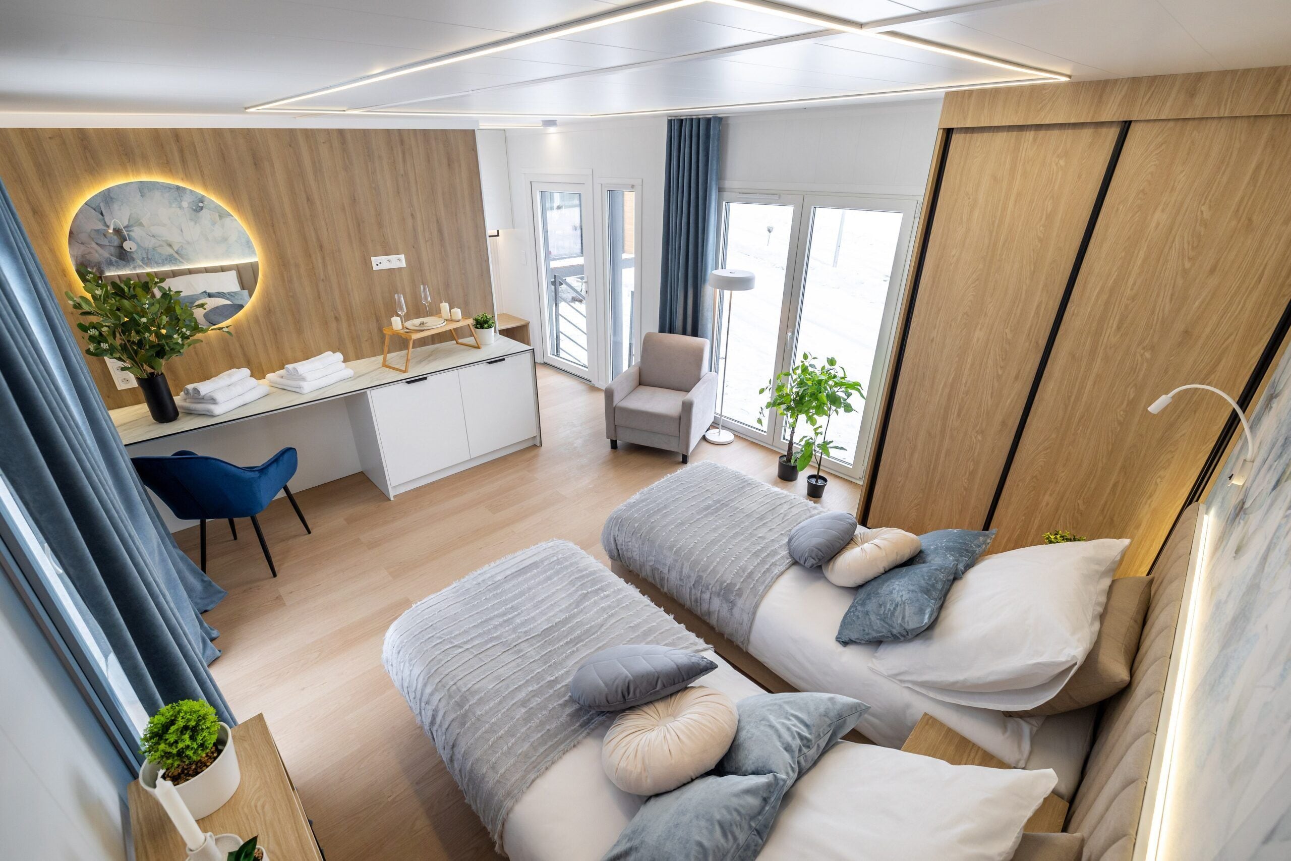 A modern hotel room with two beds, a desk, a chair, and a large window.
