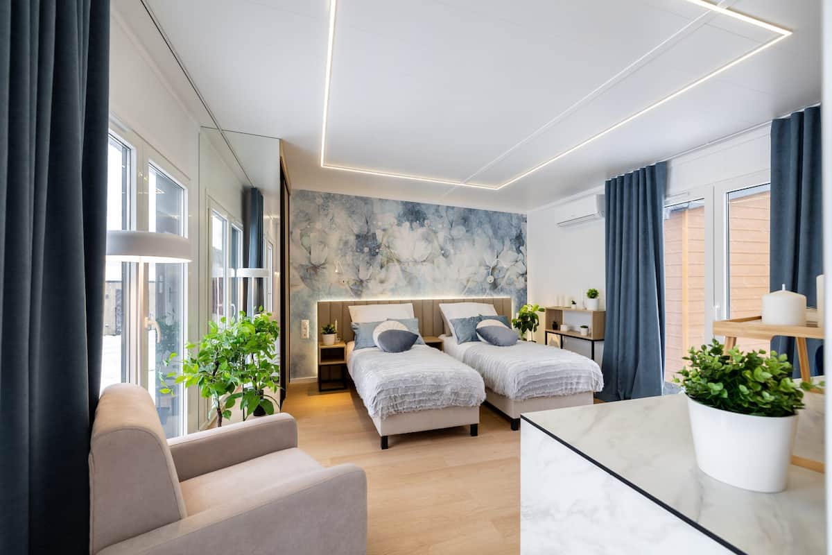 Una habitación de hotel moderna con dos camas, un sofá, una mesita de mármol y ventanas amplias.