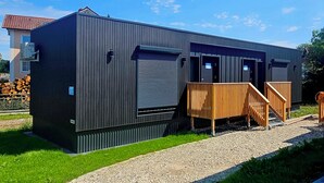 A modern building with a metal exterior, a covered entrance, and a wooden staircase leading to a platform. - Studios an der Alten Post (Maxhütte-Haidhof)