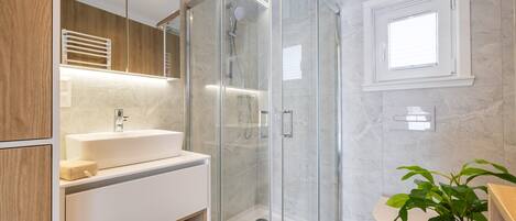 A modern bathroom with a glass-enclosed shower, a white sink, and a wooden vanity.