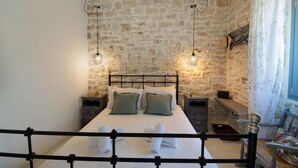 A bedroom with a stone wall, a bed with white linens, two bedside tables, and hanging light fixtures. - Malethonas Cottage by All About Paxos (Paxos)