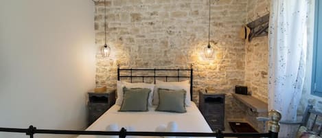 A bedroom with a stone wall, a bed with white linens, two bedside tables, and hanging light fixtures.