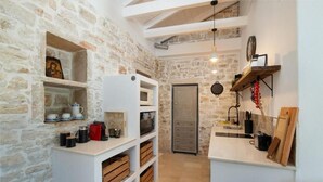 A narrow kitchen with stone walls, white cabinetry, and a wooden door. - Malethonas Cottage by All About Paxos (Paxos)