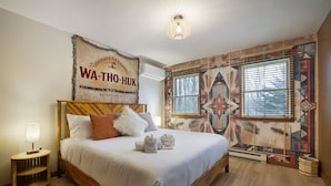 A bedroom with a bed, a nightstand, a wall tapestry, and a window with blinds.