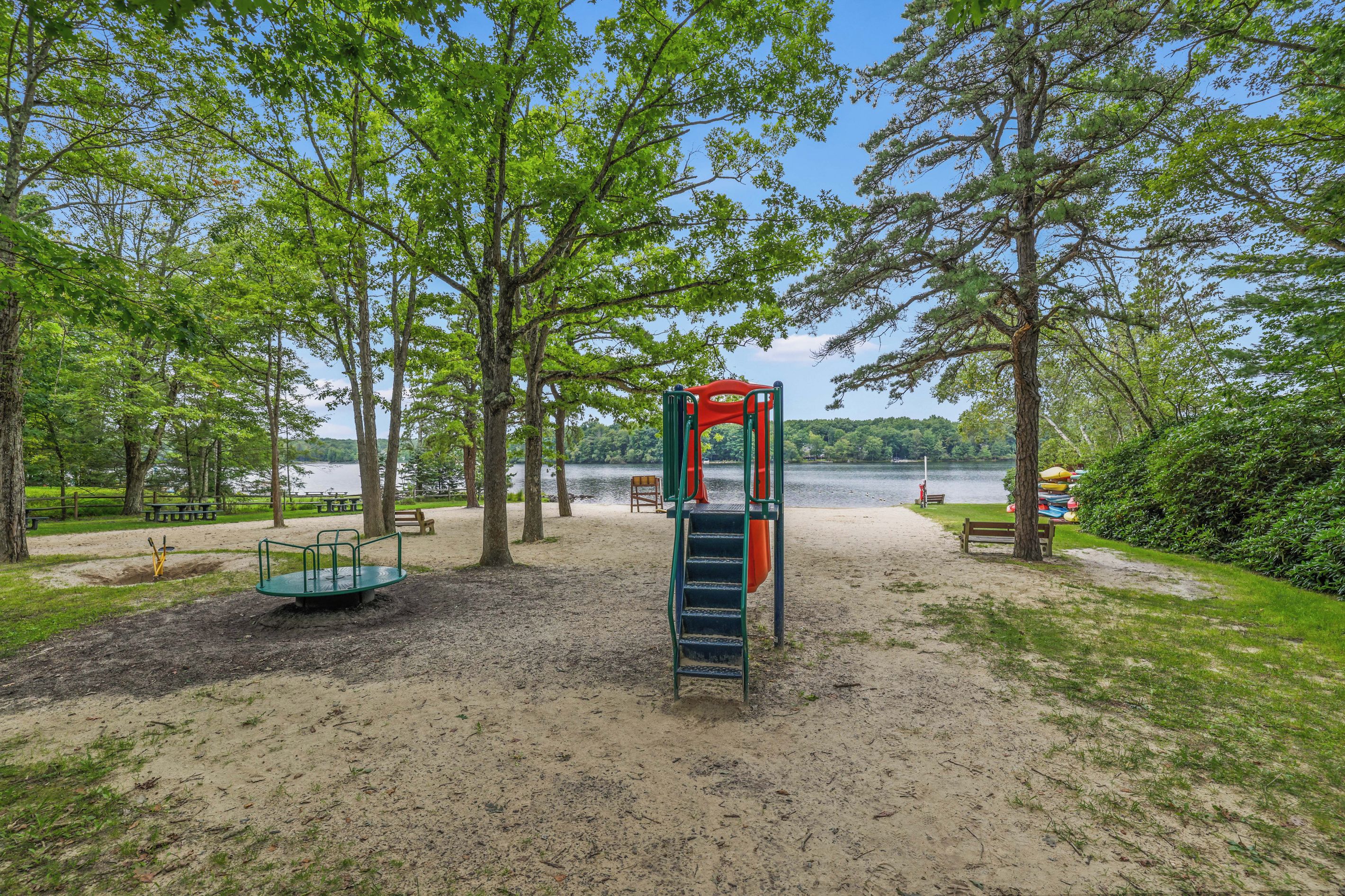 A playground with a swing set and a slide, surrounded by trees and a lake view.
