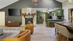 A spacious living area with a fireplace, a dining table set for four, and a kitchen with green cabinets.