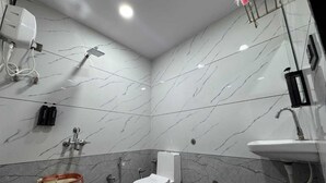 A bathroom with a toilet, shower, and sink, marble walls, and a ceiling light. - Hotel Bhujiyo Hills (Bhuj)