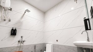 A bathroom with a toilet, shower, and sink, marble walls, and a ceiling light. - Hotel Bhujiyo Hills (Bhuj)
