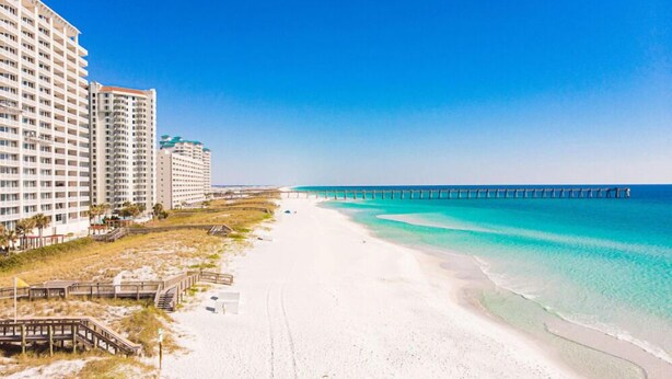 A beach with a pier, sandy shore, and high-rise buildings. - 🌊🌴Geaux Coastal | Charming 2BR Home | Steps to Private Beach Access (Navarre)