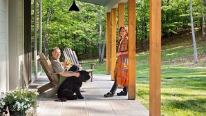 Eine überdachte Veranda mit Holzsäulen, einer Bank und einem Hund.