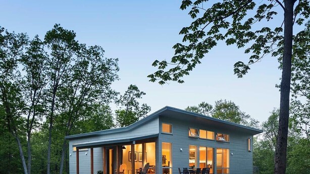 Ein modernes, zweistöckiges Haus mit überdachter Terrasse, großen Fenstern und einem Rasen.