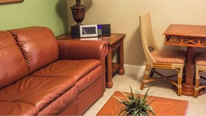 Ein Wohnzimmer mit einem braunen Ledersofa, einem kleinen Tisch mit Lampe, einer Mikrowelle und einem Korbstuhl.