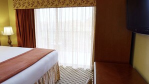 Ein Hotelzimmer mit einem Bett, einem Fernseher, einem Fenster mit Vorhängen und einer Lampe.