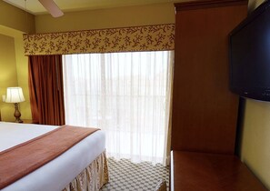 Een hotelkamer met een bed, een televisie, een raam met gordijnen en een lamp.
