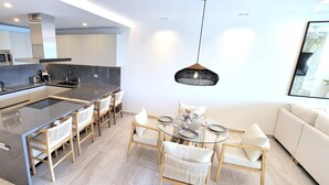Een moderne keuken met een centraal eiland, roestvrijstalen apparatuur en een eethoek met een glazen tafel en witte stoelen.