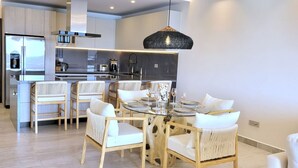 Een moderne keuken met een centraal eiland, witte stoelen en een eettafel voor zes personen.