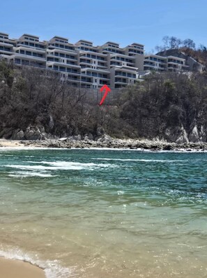 Ein Küstenhotel mit mehreren Balkonen, einer felsigen Küstenlinie und klarem, blauem Wasser.