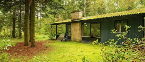Una cabaña con porche cubierto, rodeada de un bosque.