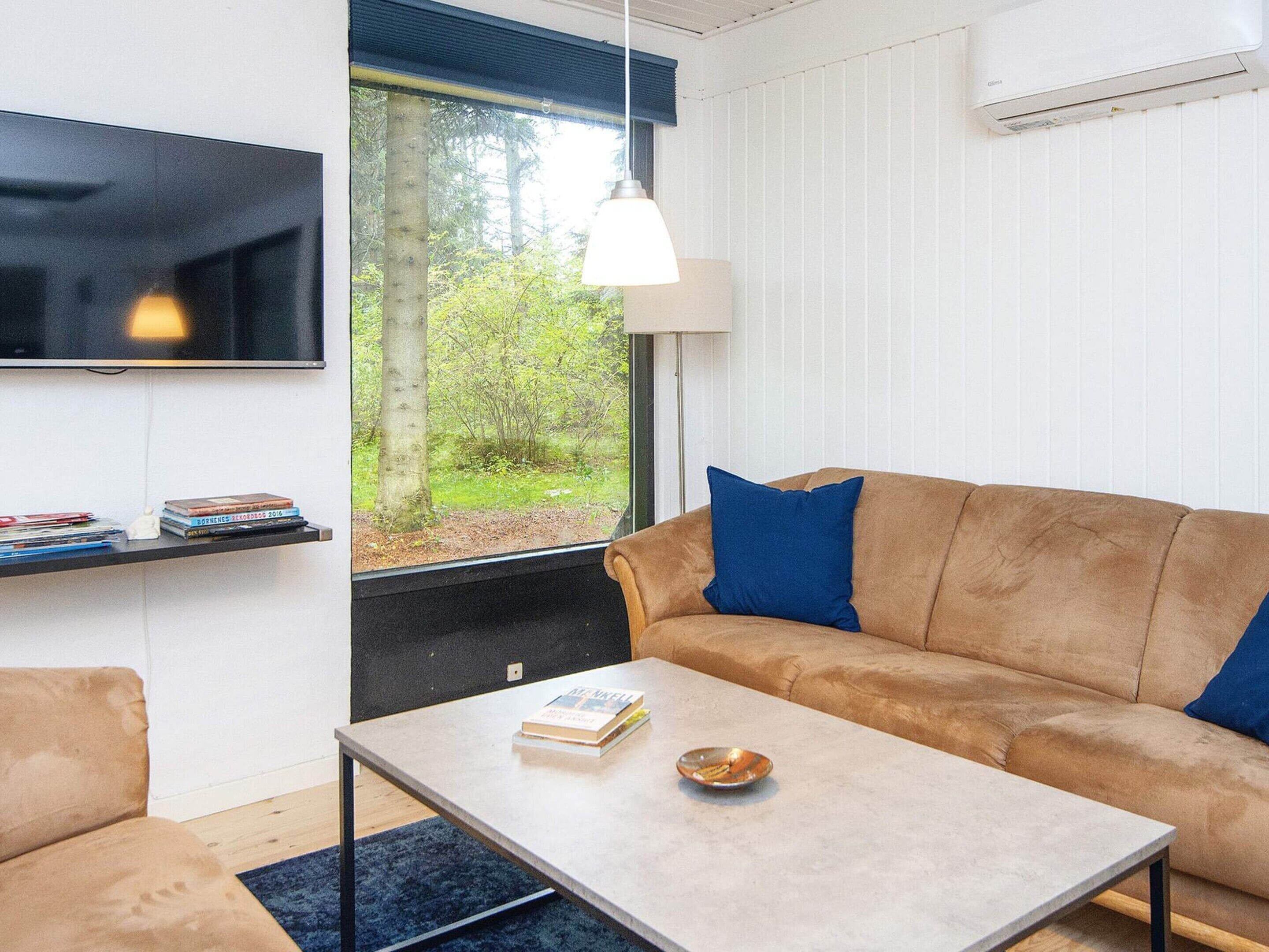 Una sala de estar moderna con un sofá, una mesa de centro, un televisor y una ventana con vistas a zonas verdes.