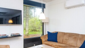 A modern living room with a sofa, a coffee table, a TV, and a window with a view of greenery. - 6 Person Holiday Home in Ans By (Ans)
