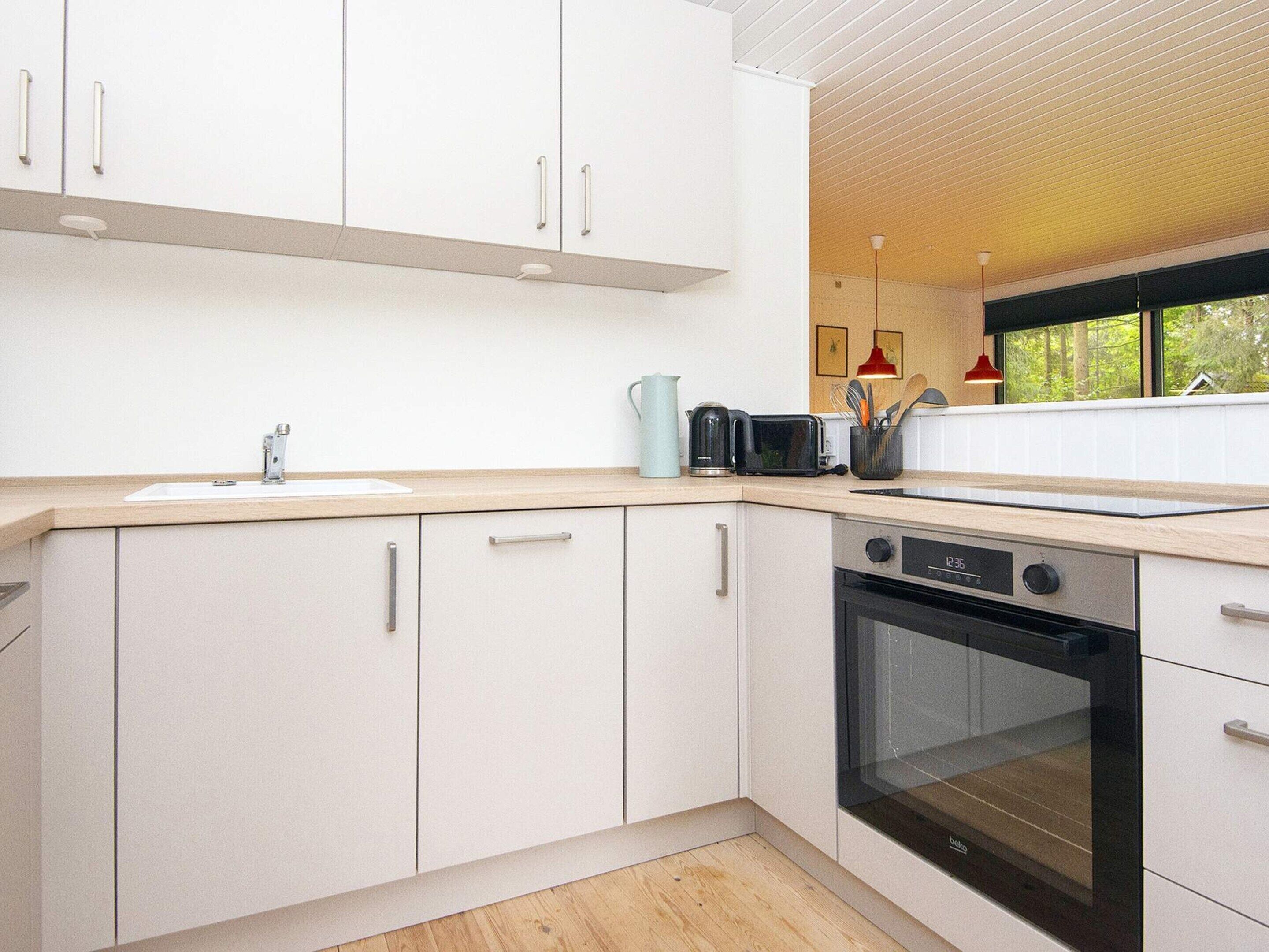 Una cocina moderna con armarios blancos, un lavamanos, una estufa y una ventana con vistas a árboles.