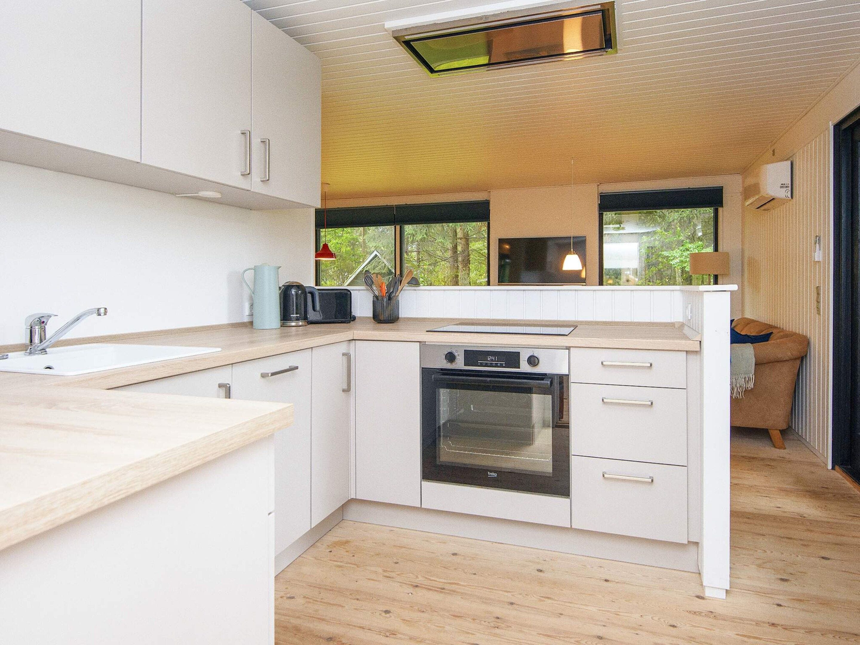 A modern kitchen with white cabinetry, a built-in oven, a sink, and a window overlooking greenery.