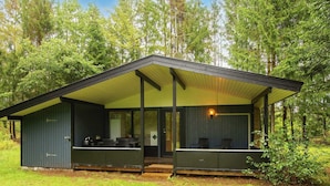 A cabin with a covered porch, a dining area, and a kitchen visible through the windows. - 6 Person Holiday Home in Ans By (Ans)