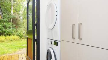 A laundry area with a washing machine and dryer, a wooden deck, and a view of a wooded area.