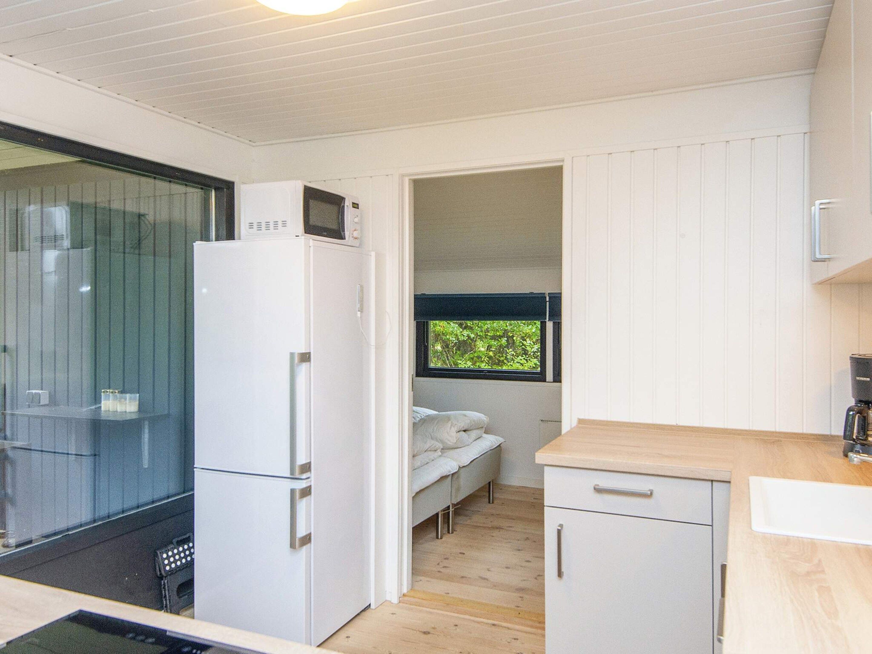 A compact kitchen with a refrigerator, a microwave, a sink, and a window with a view of greenery.