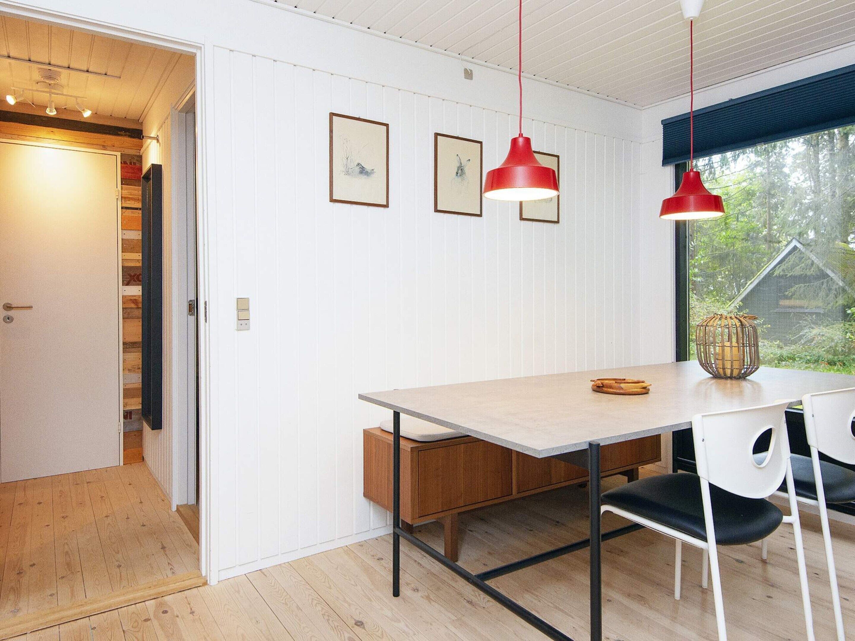 Un comedor con una mesa de madera, dos sillas, una lámpara colgante roja y cuadros en la pared.