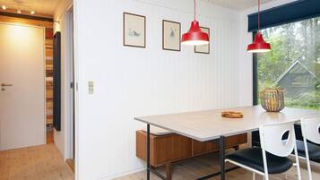 Un comedor con una mesa de madera, dos sillas, una lámpara colgante roja y cuadros en la pared.