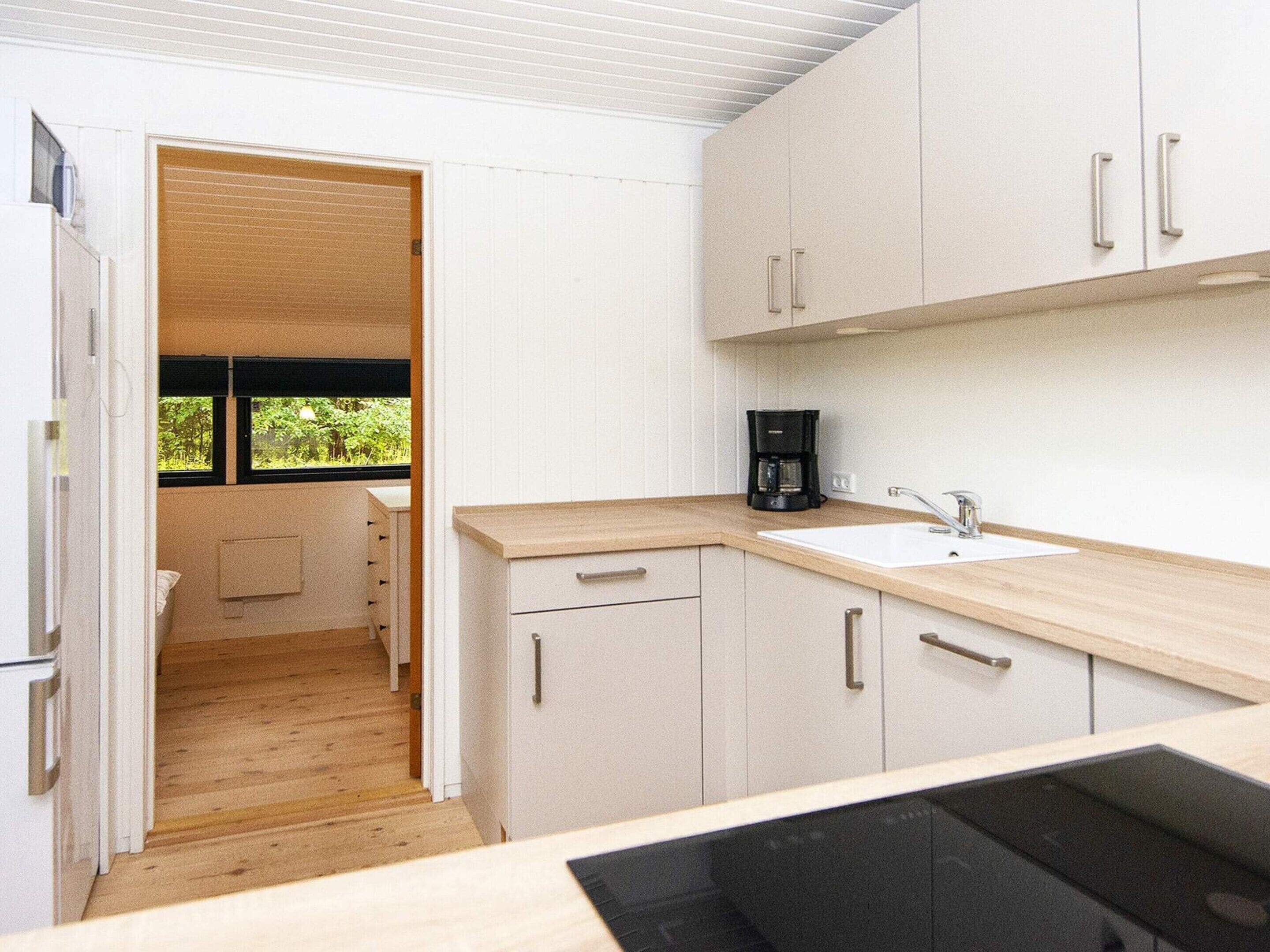 Cocina compacta con armarios blancos, encimera de madera, cafetera y ventana con vistas a zonas verdes.